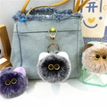 Close-up of fuzzy plush cat ball keychains with gold metal rings on a denim bag - Black