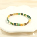 Detail shot of colorful Tila bead stretch bracelet on a white floral ceramic tray - Multicolor E-Dark Green Light Green Yellow Coffee Gold