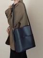 Minimalistische schwarze Leder-Eimertasche mit Henkel am Model bei natürlichem Licht - Dunkelblau
