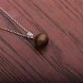 Detailed view of round tiger eye stone pendant with silver chain on dark wood background - Golden Brown (Tiger Eye)