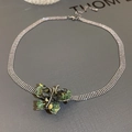Gros plan d'un collier en maille argentée avec pendentif papillon en cristal vert - Vert
