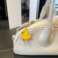 Detail of a yellow enamel duck charm with gold hook hanging on a white leather bag - Yellow Duck