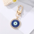 Macro shot of evil eye keychain with blue enamel and white rhinestones on white stones - Rhinestone Enamel Round Blue Eye