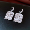 Dettaglio degli orecchini in argento con trama stropicciata su pelle nera elegante - Stile Quadrato Piegato Irregolare / Argento