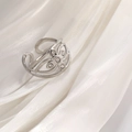 Detailed shot of a silver hollow flower ring with diamonds on white silk fabric - Silver Tone Zirconia Flower