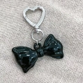 Detail of glossy black acrylic bow keychain with silver heart clasp on gray knit background - Horizontal Black Bowknot Style (M322横版黑蝴蝶结)