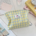 Detalle del neceser de lona a cuadros amarillos y azules con etiqueta tejida en mesa - Amarillo