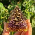 Macro shot of an Orgone pyramid with a gold Buddha statue and amethyst crystals held by hand - Style 7