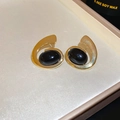 Detailansicht der goldenen geometrischen Oval-Ohrringe mit schwarzen Steinen auf Stoff - Gold (Stahlstift)