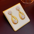 Dettaglio di orecchini vintage dorati con perle a goccia e fiori su supporto beige - Perno d'Argento-Oro Set da 3 Pezzi