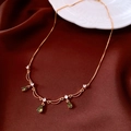 Close-up of 18k gold plated necklace with green teardrop pendants on dark red fabric - Necklace / Gold with Green Gemstone