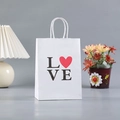 White kraft gift bag with heart LOVE print and twisted paper handles on a minimalist table - 116-2 White LOVE Heart