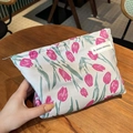 Beige canvas makeup bag with pink tulip print and woven label in a hand-held view - Rose Red Tulip