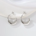 Detailed view of polished silver C-shape hoop earrings on a white silk backdrop - 1180 Steel Color Crescent