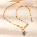 Detail van vergulde Hamsa hand ketting met blauw emaille en zirkoon op zijden stof - Gouden Hand van Fatima