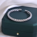 Detailansicht eines silbernen geflochtenen Mesh-Armreifs auf einer Geschenkbox - Stahlfarbe