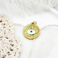 Macro view of gold evil eye charm with blue enamel on white feather background - Eye Round Disc