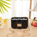 Mini-Gelee-Tasche in Schwarz mit Steppmuster und Goldkette auf einer Holzoberfläche - Schwarz