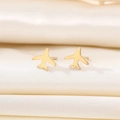 Minimalist gold airplane stud earrings displayed on elegant ivory silk fabric - Gold