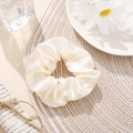 Detail view of cream satin scrunchie on woven mat with vintage aesthetic props - Ivory