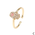 Detailed macro of golden Hamsa Hand ring featuring red enamel evil eye and zircon stones - Adjustable Open / Red Eye