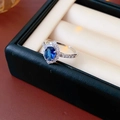 Makroaufnahme eines silbernen Rings mit blauem Saphir und einem weißen Zirkonia-Halo - Offener Ring - Silber / Blau Raute