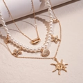 Detail einer mehrlagigen Goldkette mit weißen Perlen, Seestern- und Muschel-Anhängern - Gold