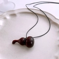 Détail d'un pendentif gourde en bois vintage sur cordon noir posé sur une assiette blanche - Rouge