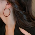 Primo piano di una modella che indossa orecchini a cerchio in smalto bordeaux e oro - Grande Cerchio Rosso Torsonata in Smalto (2#)