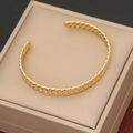 Detail of a golden twisted rope bangle placed on a beige jewelry box with metallic finish - Gold Twisted Rope Texture Open Cuff Style (4#)