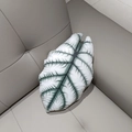 Detail of grey-green plush leaf pillow showing realistic Alocasia veins on a leather sofa - White Rhino