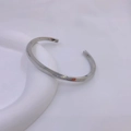 Close-up of polished silver Mobius twist cuff bracelet on a minimalist white stand - Steel