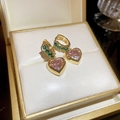 Macro shot of gold hoop earrings with green stones and pink heart zircon pendants - Heart Zirconia Huggie / Gold Inlaid with Green and Pink Zirconia