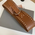 Dettaglio della cintura in pelle caramello con borchie argentate e fibbia rotonda in metallo - Caffè Scuro