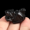 Miniature black crystal stone squirrel carving held between fingers to show compact size - Obsidian