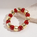 Dettaglio macro di un bracciale con perle rosse glitterate e cubi dorati su pietra - Rosso