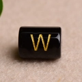 Macro shot of a black cylindrical bead featuring a gold-engraved letter W for DIY jewelry - Letter W