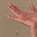 Vue détaillée du pendentif perle en forme de goutte sur une chaîne argentée en main - Argent-Perle