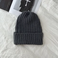 Detailed close-up of dark grey thick vertical striped knitted beanie on a soft white cloth - Gray