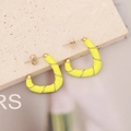 Detailed shot of yellow enamel earrings with golden metal wire on a stone background - Yellow