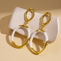Detail van geometrische gouden en witte emaille oorbellen op een keramische standaard - Goud