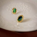 Détail de boucles d'oreilles dorées irrégulières avec incrustations vertes irisées - Doré