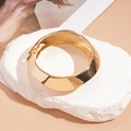 Detailopname van een dikke gouden geometrische metalen armband op een witte stenen basis - Gouden Ronde Open Armband