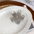Detailed view of a transparent grey flower hair claw clip on a white ceramic plate - Gray