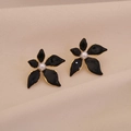 Detail of black enamel flower earrings with gold edges and center pearl on beige fabric - Black