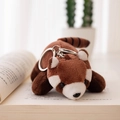 Cute red panda plush keychain pendant with striped tail laying on an open book - Charm / Brown