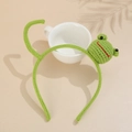Detailed view of a green hand-knitted frog headband for kids on a ceramic cup base - Frog