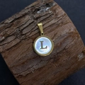 Golden round sea shell pendant with letter L inlay on a natural wood surface - Letter L / 17x20mm