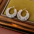 Detalle de pendientes de aro plateados con brillantes sobre un fondo de tela verde - Plateado