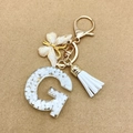 Handmade letter G resin keychain with gold butterfly charm and white tassel on brown background - Letter G